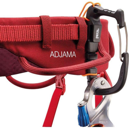 A close-up of the Petzl Adjama dark red climbing harness showing the buckle and carabiner attachment points.