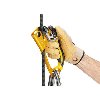 A hand wearing a tan glove holds the yellow Petzl Ascension Right ascender against a black climbing rope.