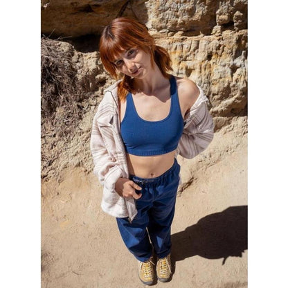 A woman wearing the Prana Sample - Women's Tornado Bra in Capulet Blue stands in front of rocky terrain.
