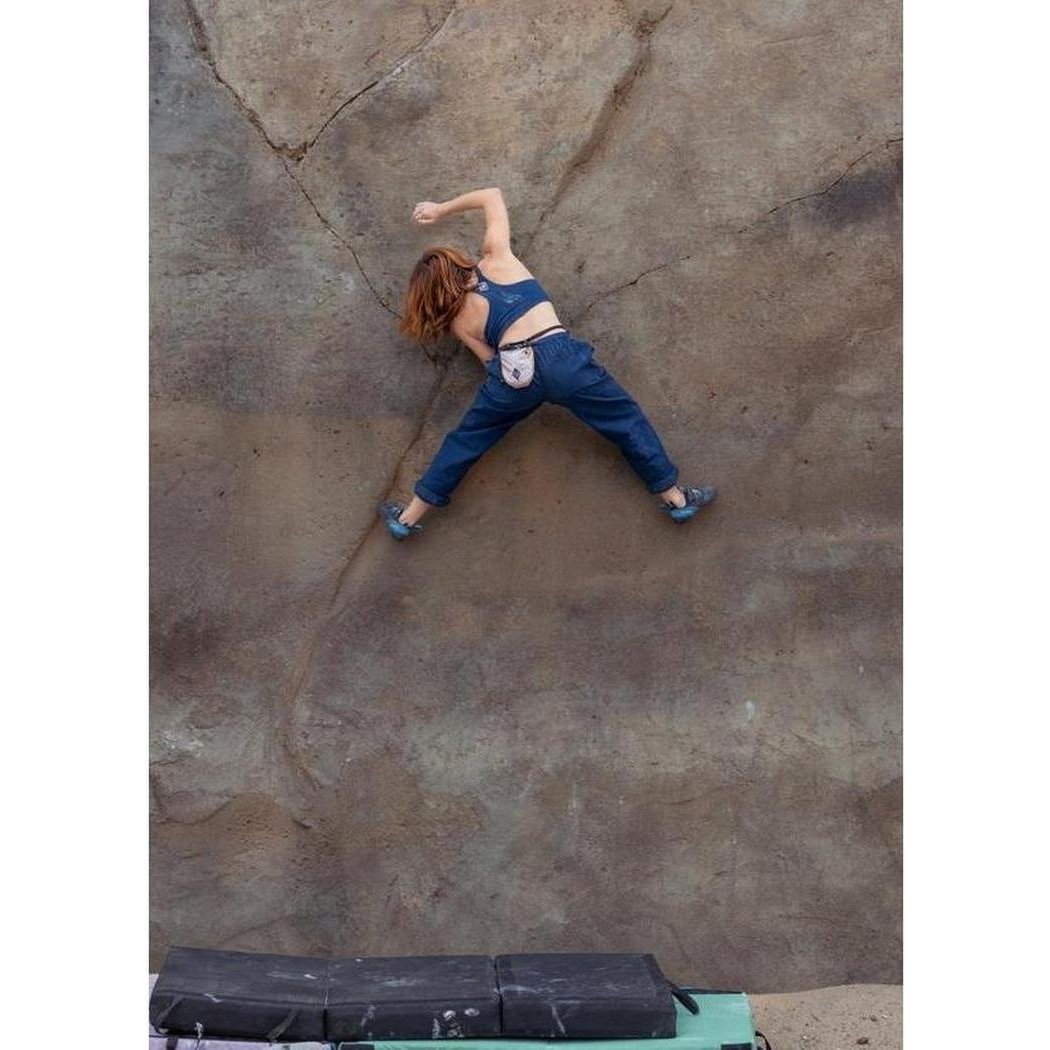 A woman climbs a rock face wearing the Prana Sample - Women's Tornado Bra in Capulet Blue.