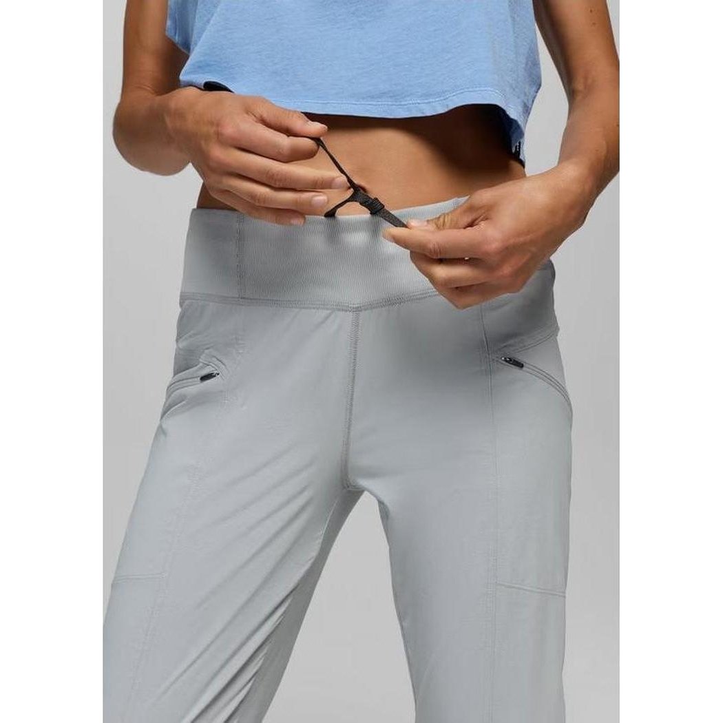 A model wearing the Prana Women's Koen Mid Rise Daily Pant in Grey Blue adjusts the waistband against a plain background.