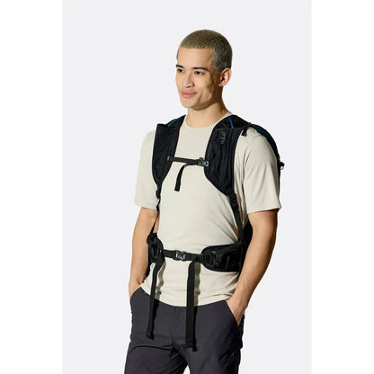 A man wearing the Rab Airox 24 backpack in Tempest Blue stands against a plain white background.