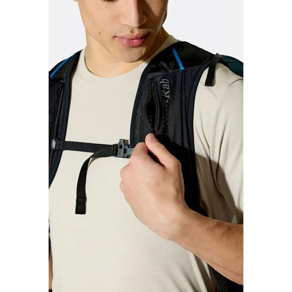 A model wearing the Rab Airox 24 backpack in Tempest Blue adjusts a strap against a white background.