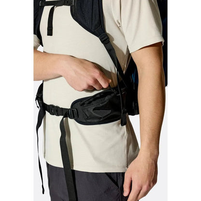A model wearing the Rab Airox 24 backpack with a Tempest Blue panel and black straps, showing the waist belt pocket.