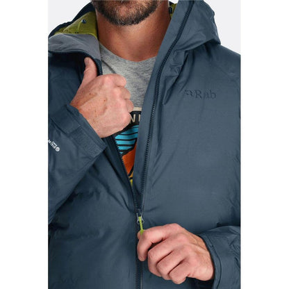 A man wearing the Rab Men's Valiance Jacket in Black adjusts the zipper while giving a thumbs up.