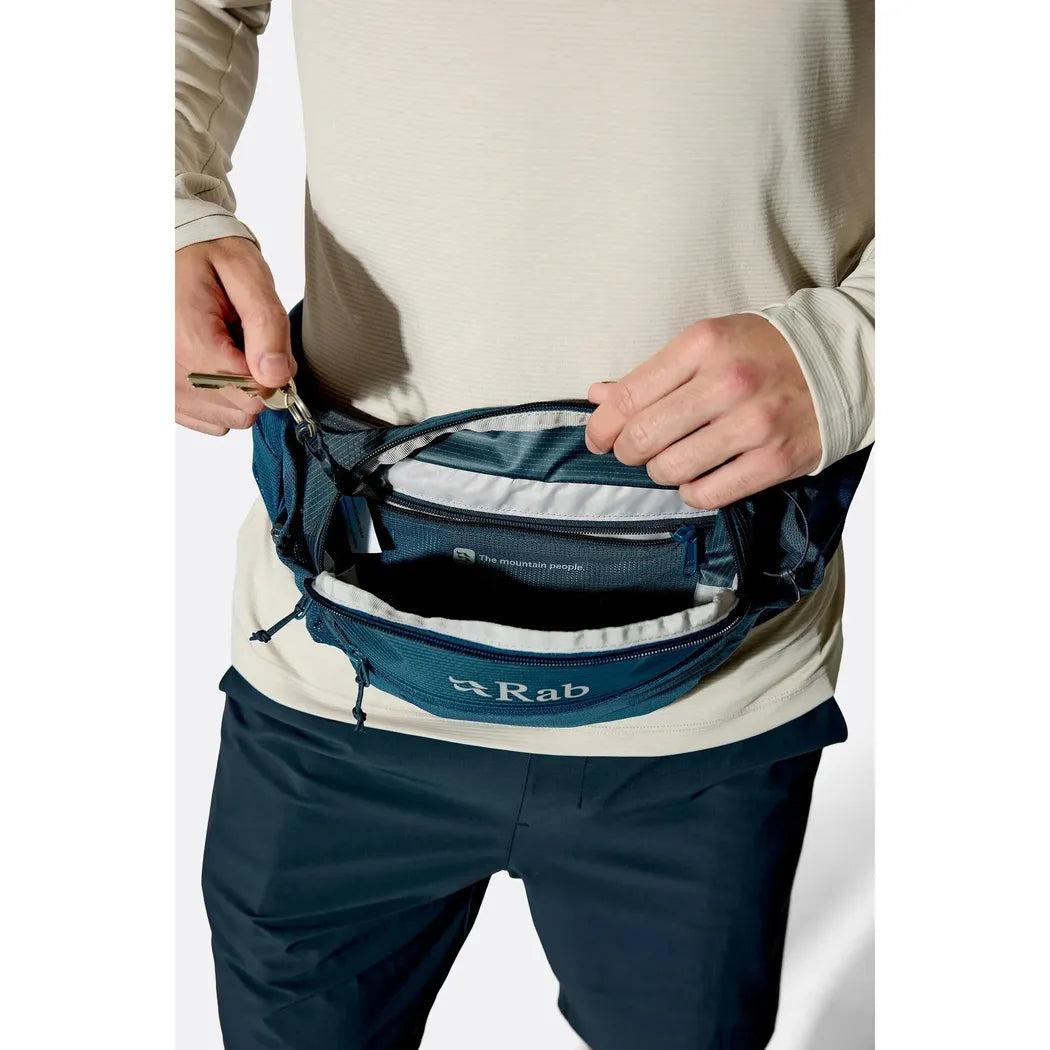 A model wearing the Rab Protium 6 waist pack in Anthracite opens the main compartment against a white background.