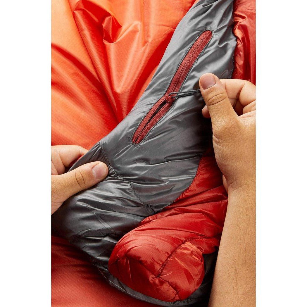 A person holds the Rab Solar Eco 4 sleeping bag in Firecracker color, showing the charcoal interior and red zipper.