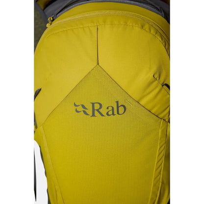 A close-up of the yellow Rab Tygen 12 backpack showing the brand logo and a zippered top pocket.