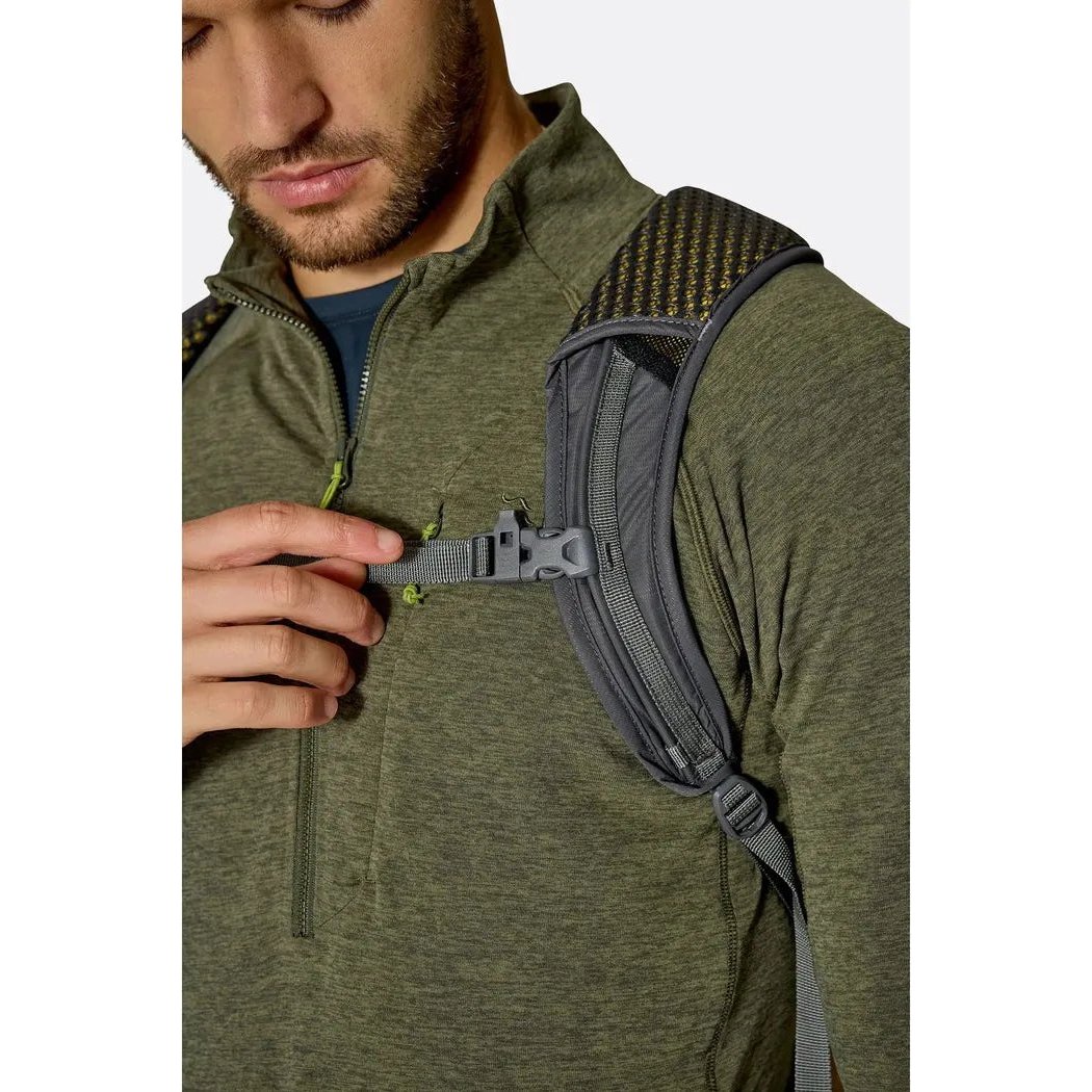 A model wearing the Rab Tygen 12 daypack in Black adjusts a strap on the shoulder strap.