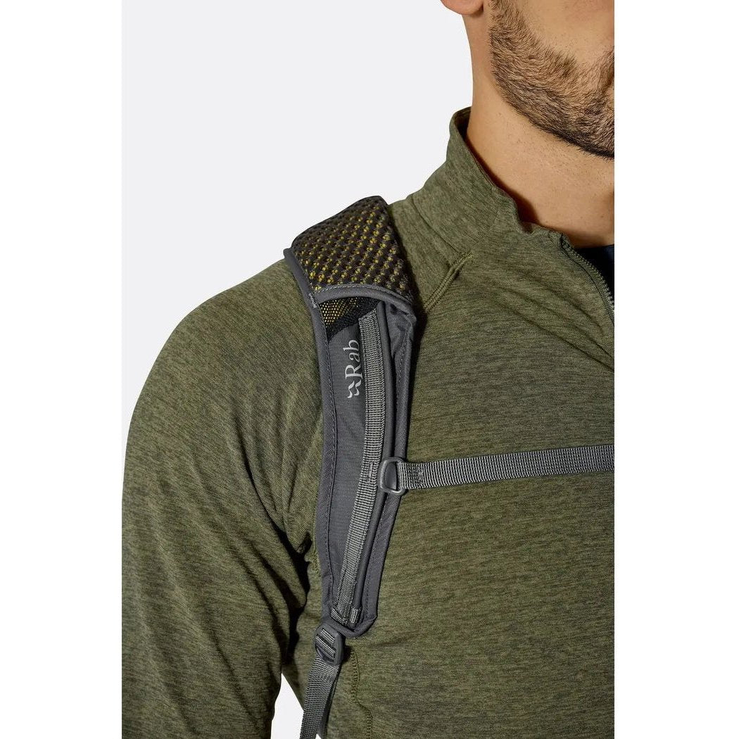 A close-up of a man wearing the Rab Tygen 12 backpack in Black, showing the shoulder strap and mesh padding against a plain white background.