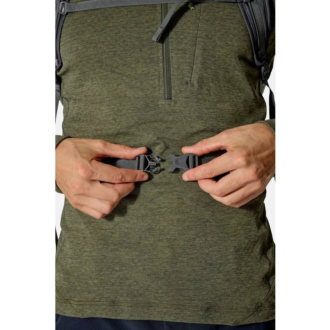 A close-up of the Rab Tygen 12 backpack in Black, showing a model fastening a belt buckle on their waist.