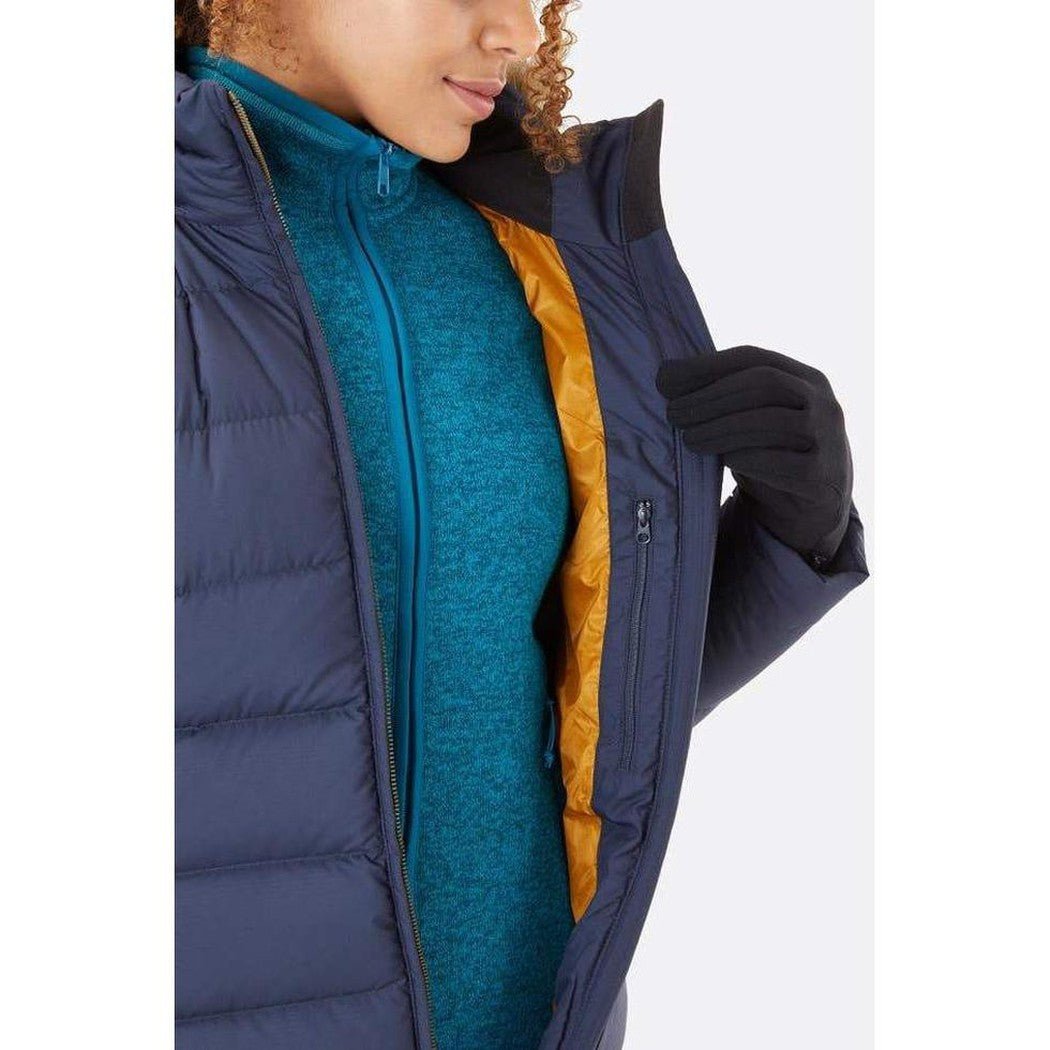 A model wears the Rab Women's Deep Cover Parka in Army color, showing the zipper and interior lining against a white background.