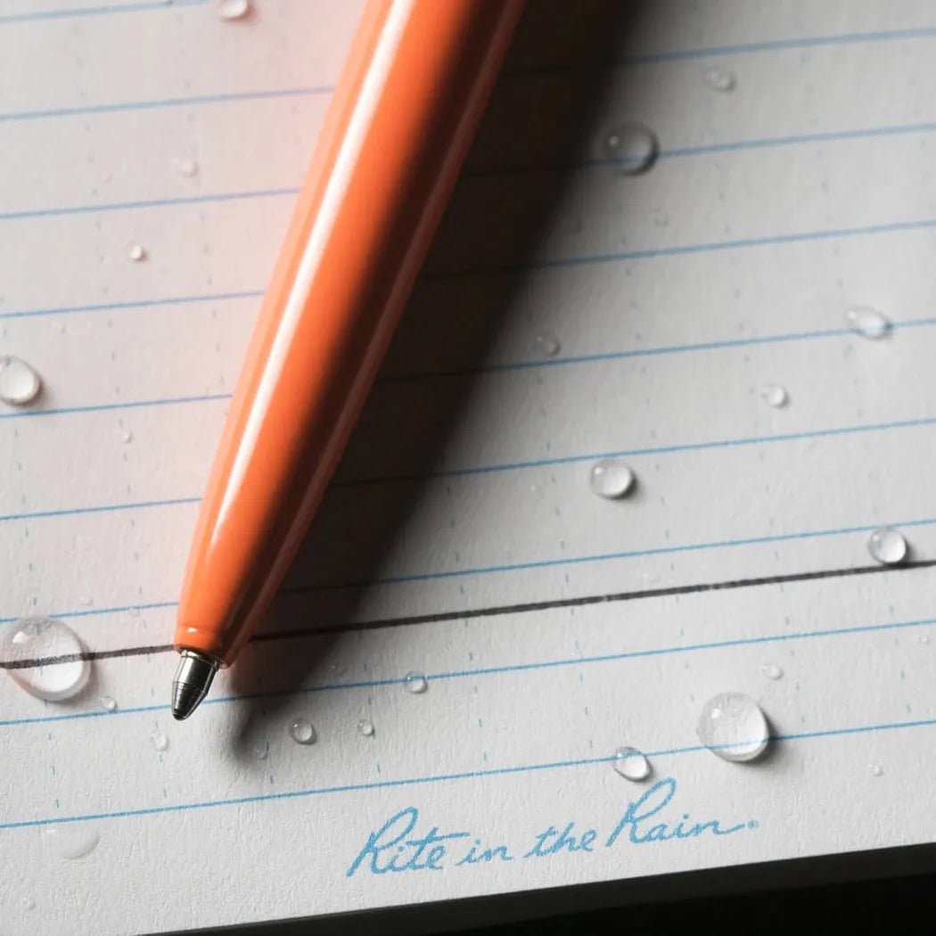 A close-up of the black Rite in the Rain All-Weather Metal Pen on lined paper with water droplets.