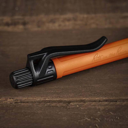 A close-up of the Rite in the Rain Click Action Pen in Orange on a wooden surface.