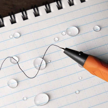 A close-up of the Rite in the Rain Click Action Pen in Orange writing on a lined notebook with water droplets.