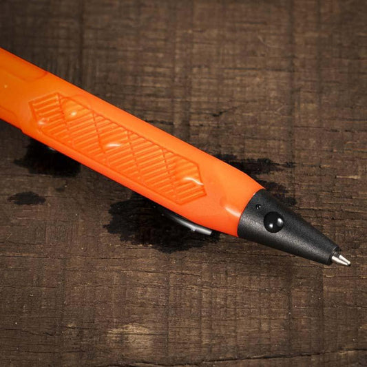 A close-up of the Rite in the Rain Click Action Pen in Orange lying on a dark wooden surface.