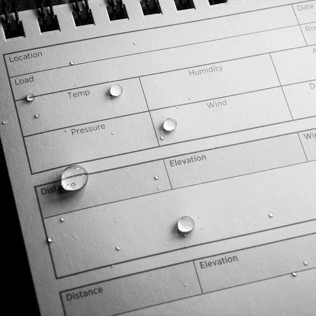 A close up of the Rite in the Rain Dope Logbook - Top Spiral 4x6 showing water droplets on the black pages.