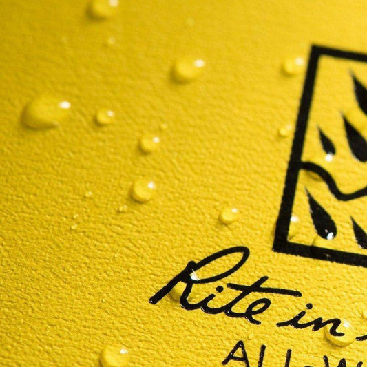 A close-up of a yellow Rite in the Rain hard cover book with water droplets on its surface.
