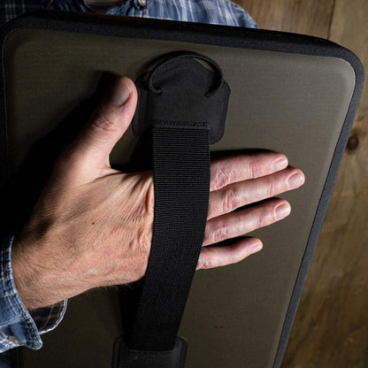 A hand holds the Rite in the Rain Monsoon Field Desk, showing its black strap and clamp feature against a wooden background.