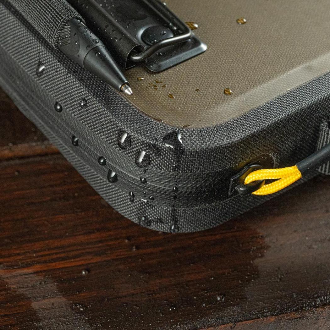 A close-up of the Rite in the Rain Monsoon Hand Desk in Dark Green, showing water droplets on its surface and a yellow pull tab.