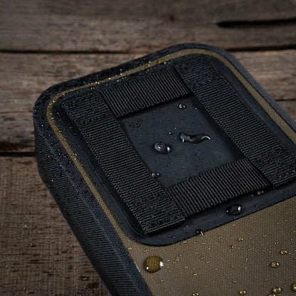 A close-up of the Rite in the Rain Rain Shadow Utility Pouch in Dark Green, showing water droplets on its surface against a wooden background.