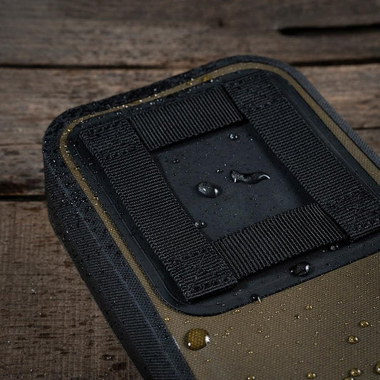 A close-up of the Rite in the Rain Rain Shadow Utility Pouch in Dark Green, showing water droplets on its surface against a wooden background.