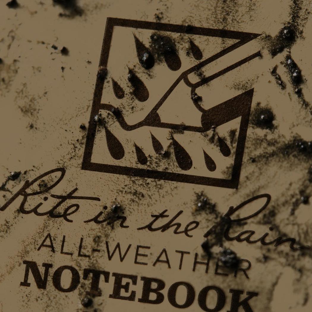 A close up of the Rite in the Rain notebook showing the all weather logo and text on a dirty background.