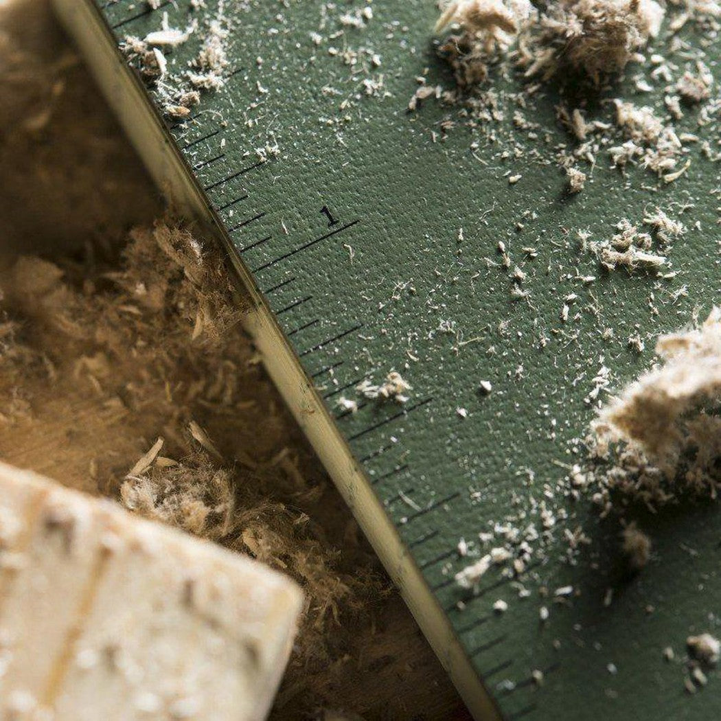 A close-up of the black Rite in the Rain Soft Cover Book on a green ruler with wood shavings around it.