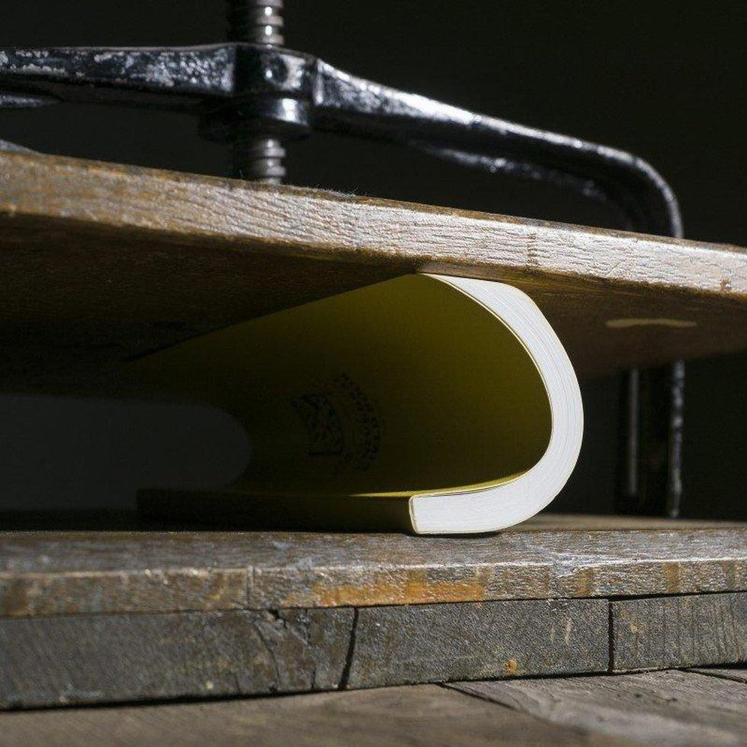 A close-up of the Rite in the Rain Soft Cover Book in Black, showing the book under a metal press on a wooden surface.