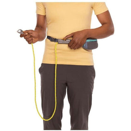 A person wearing a yellow shirt and charcoal pants holds the Ruffwear Hitch Hiker Leash with a yellow cord and Aurora Teal pouch against a white background.
