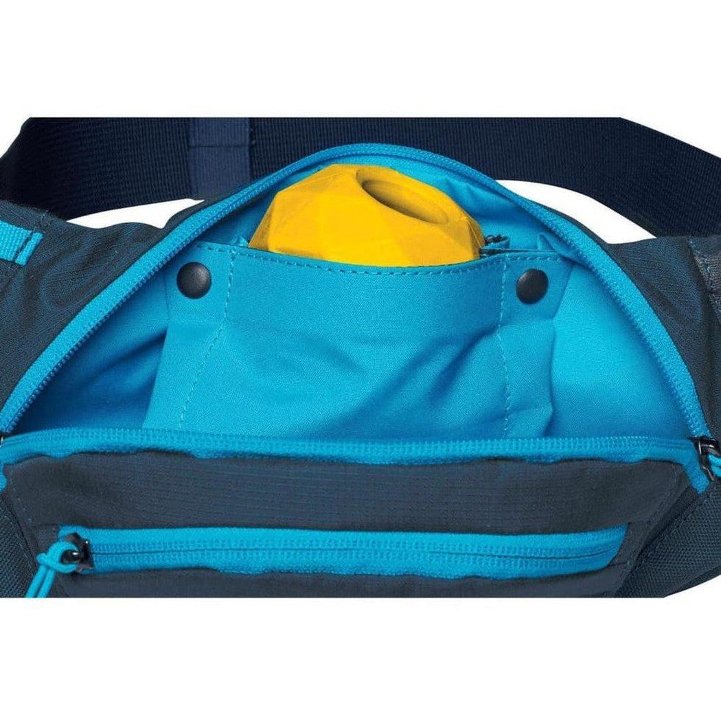 A close-up of the Ruffwear Home Tail Hip Pack in Aurora Teal showing the front pocket with a yellow item inside and a zippered compartment below.