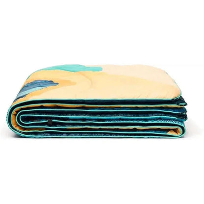 A folded Rumpl Original Puffy - Ridgeline Views blanket with a colorful design, showing its layers and edges against a white background.