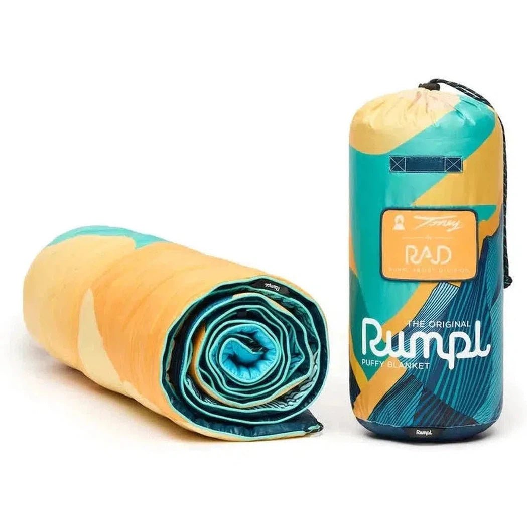 A rolled-up Ridgeline Views Rumpl Original Puffy blanket next to its yellow and teal storage bag on a white background.