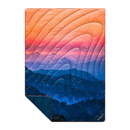A Rumpl Original Puffy blanket in Alpenglow color shows a mountain sunset design with a folded corner visible.