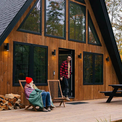 A woman in a red hat sits on a deck chair with a Deepwater Rumpl Sherpa Puffy blanket, while a man in a red plaid shirt stands at the cabin door.