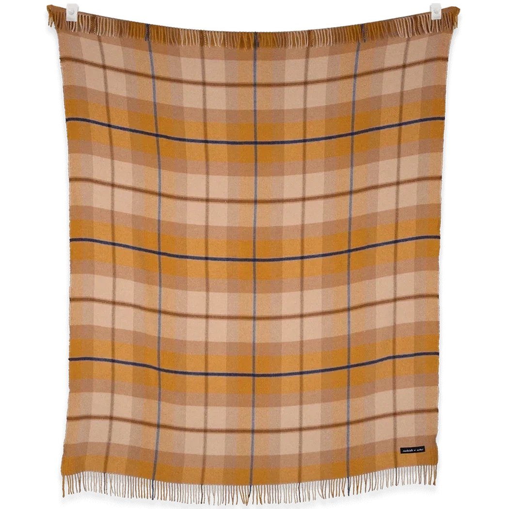 A close-up of the Sackcloth & Ashes Folk Collection Amber blanket with fringes, hanging against a white background.