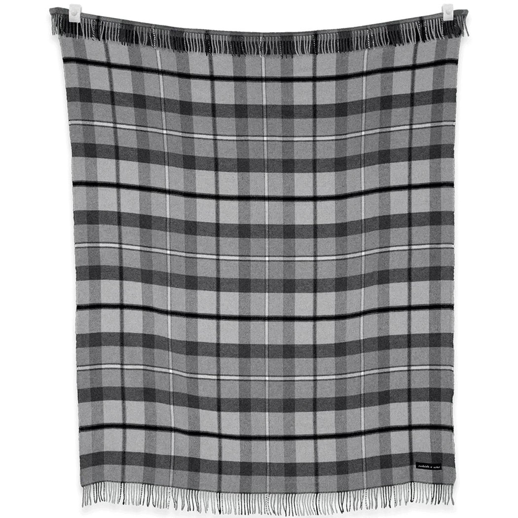 A charcoal and graphite plaid blanket from the Sackcloth & Ashes Folk Collection hangs on a clothesline with fringes visible.
