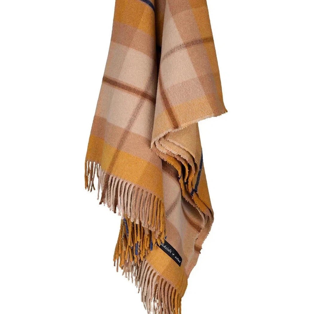 A folded Amber Sackcloth & Ashes Folk Collection blanket with fringes hangs against a white background.