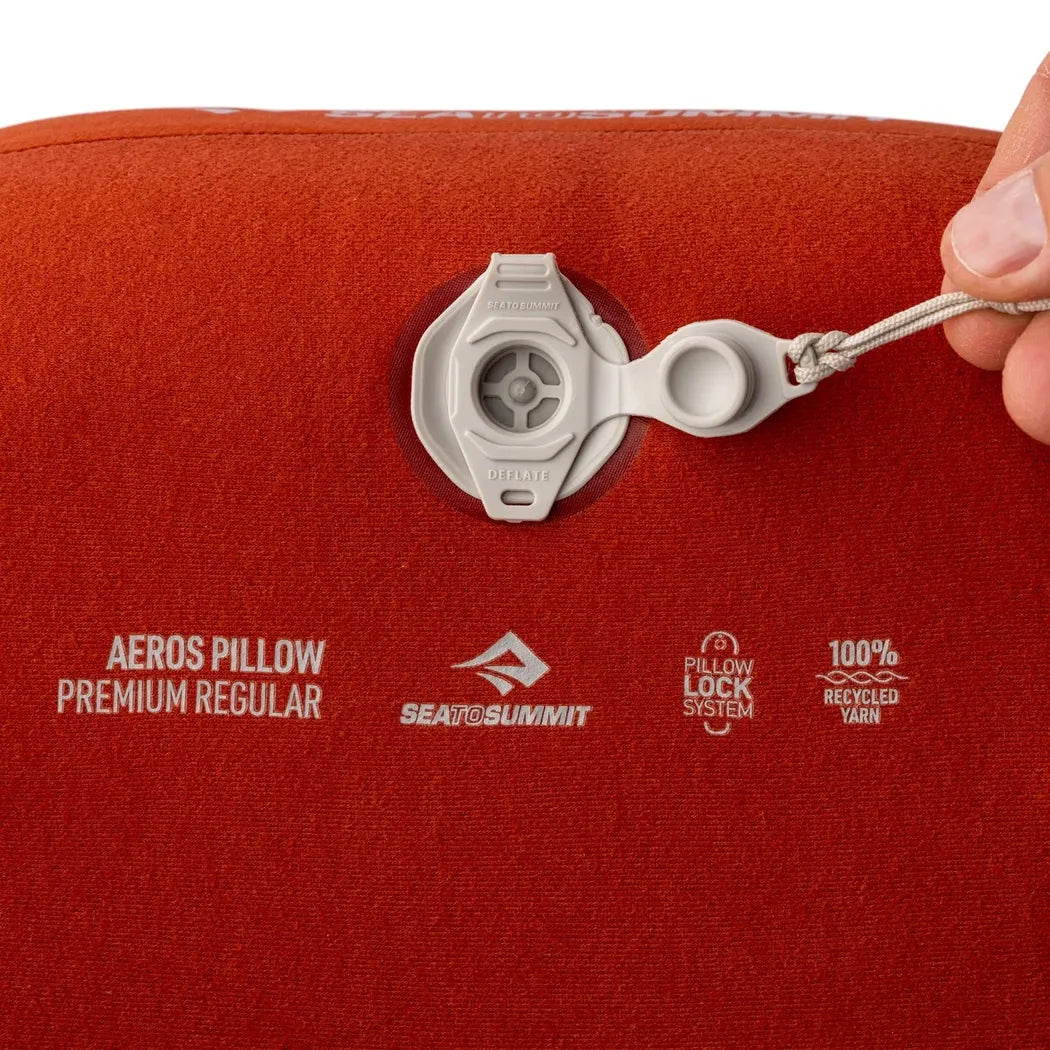 A close-up of the Sea To Summit Aeros Premium Pillow in Burnt Olive showing the pillow lock system and a hand adjusting the valve.