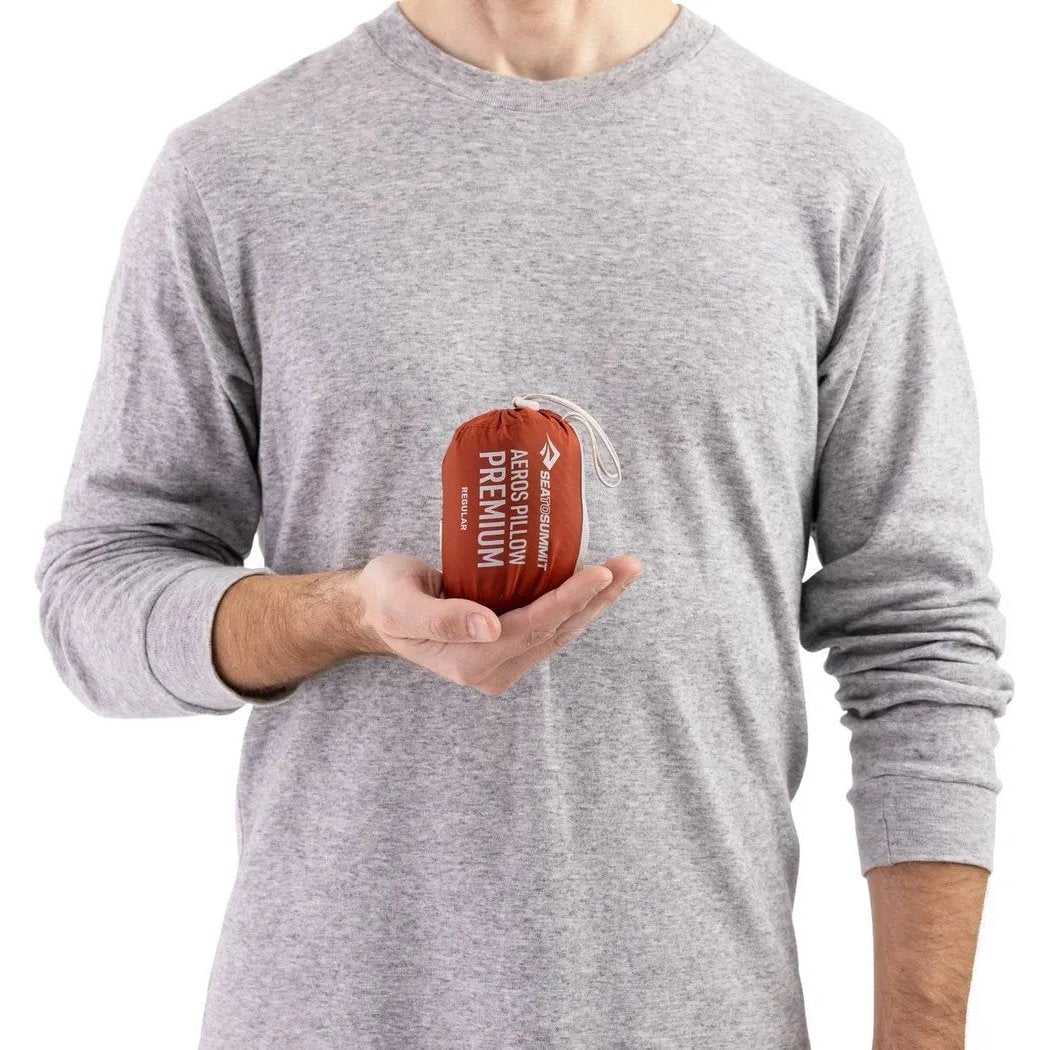 A person in a gray shirt holds the Sea To Summit Aeros Premium Pillow in their hand against a white background.