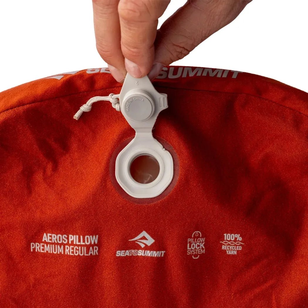 A hand adjusts the valve on a red Sea To Summit Aeros Premium Pillow against a white background.