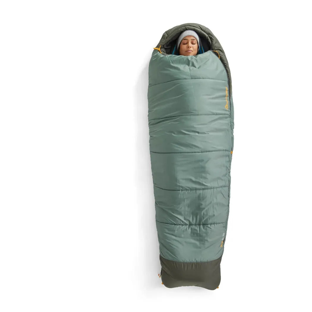 A person wearing a gray beanie is inside the Sea To Summit Boab Synthetic Sleeping Bag 30F|-1C, which is Laurel Wreath Green with a dark gray bottom, shown from a top-down angle against a white