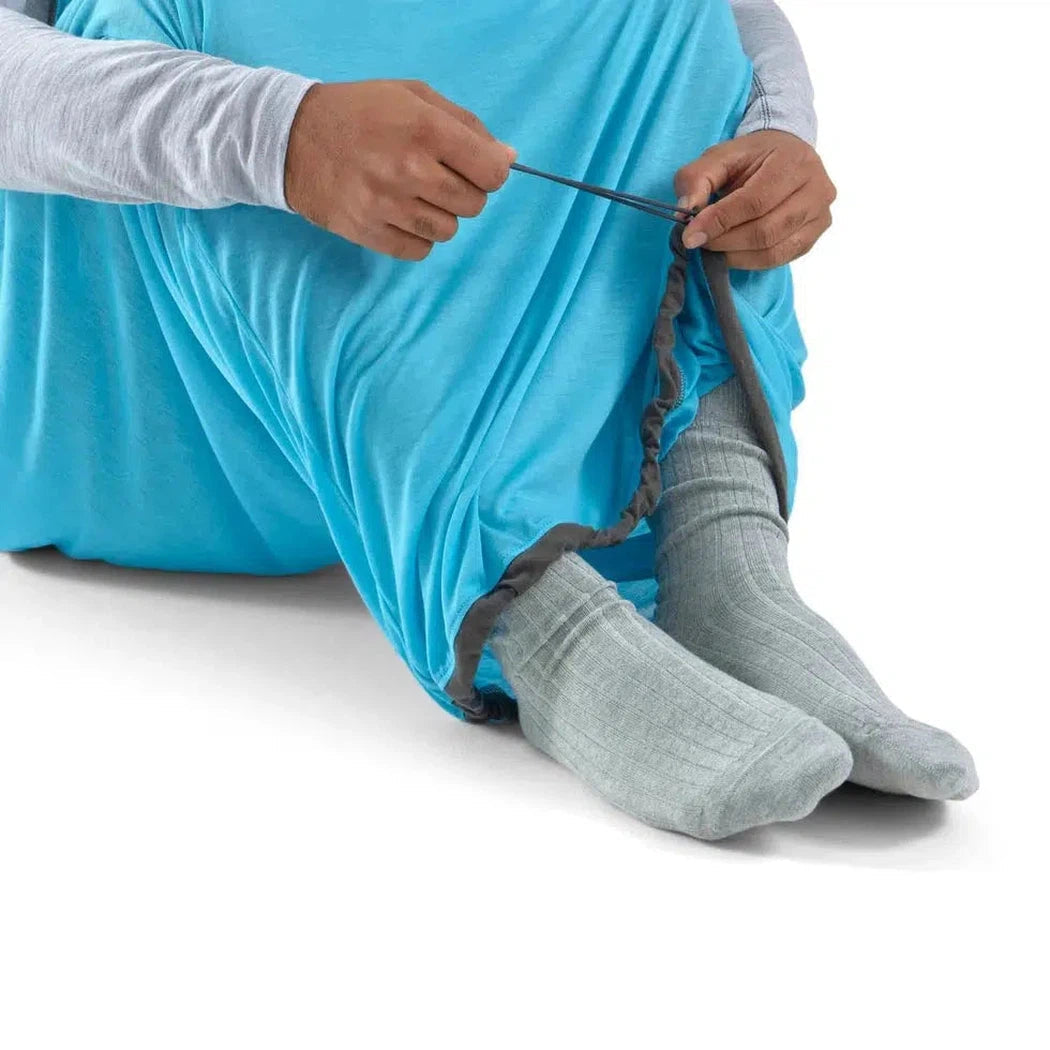 A person sits wearing the Sea To Summit Breeze Sleeping Bag Liner in Blue Atoll, showing the leg opening and elastic drawstring against a white background.