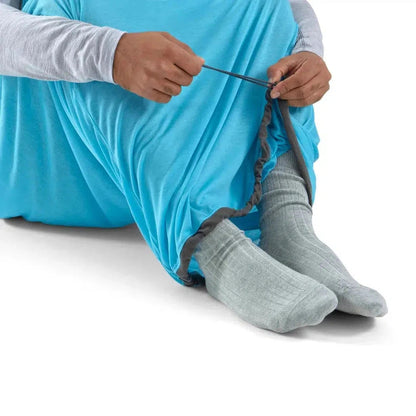 A person sits wearing the Sea To Summit Breeze Sleeping Bag Liner in Blue Atoll, showing the leg opening and elastic drawstring against a white background.