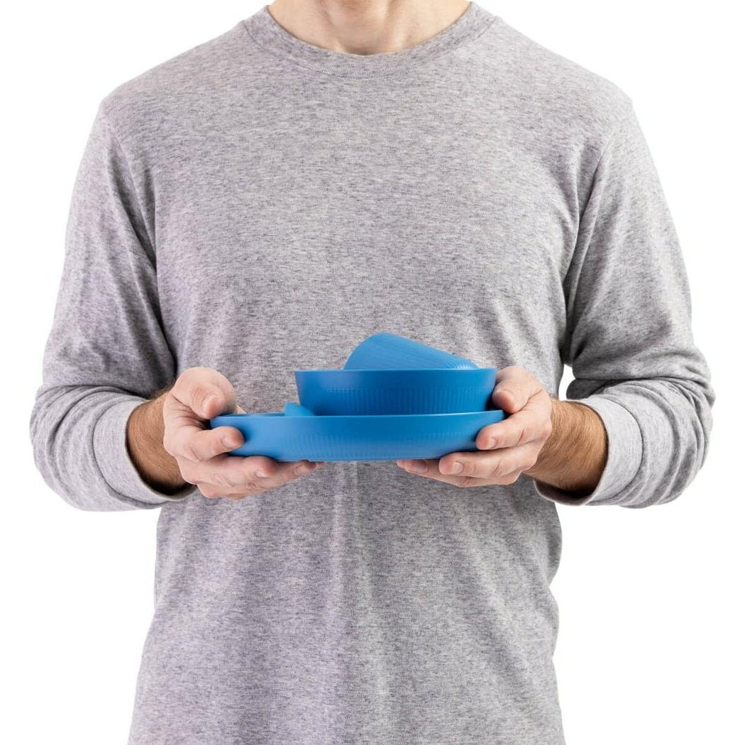 A person wearing a gray long-sleeve shirt holds the Burnt Orange Sea To Summit Camp Dinnerware Set w/ Mesh Sack - [6 Piece] against a white background.