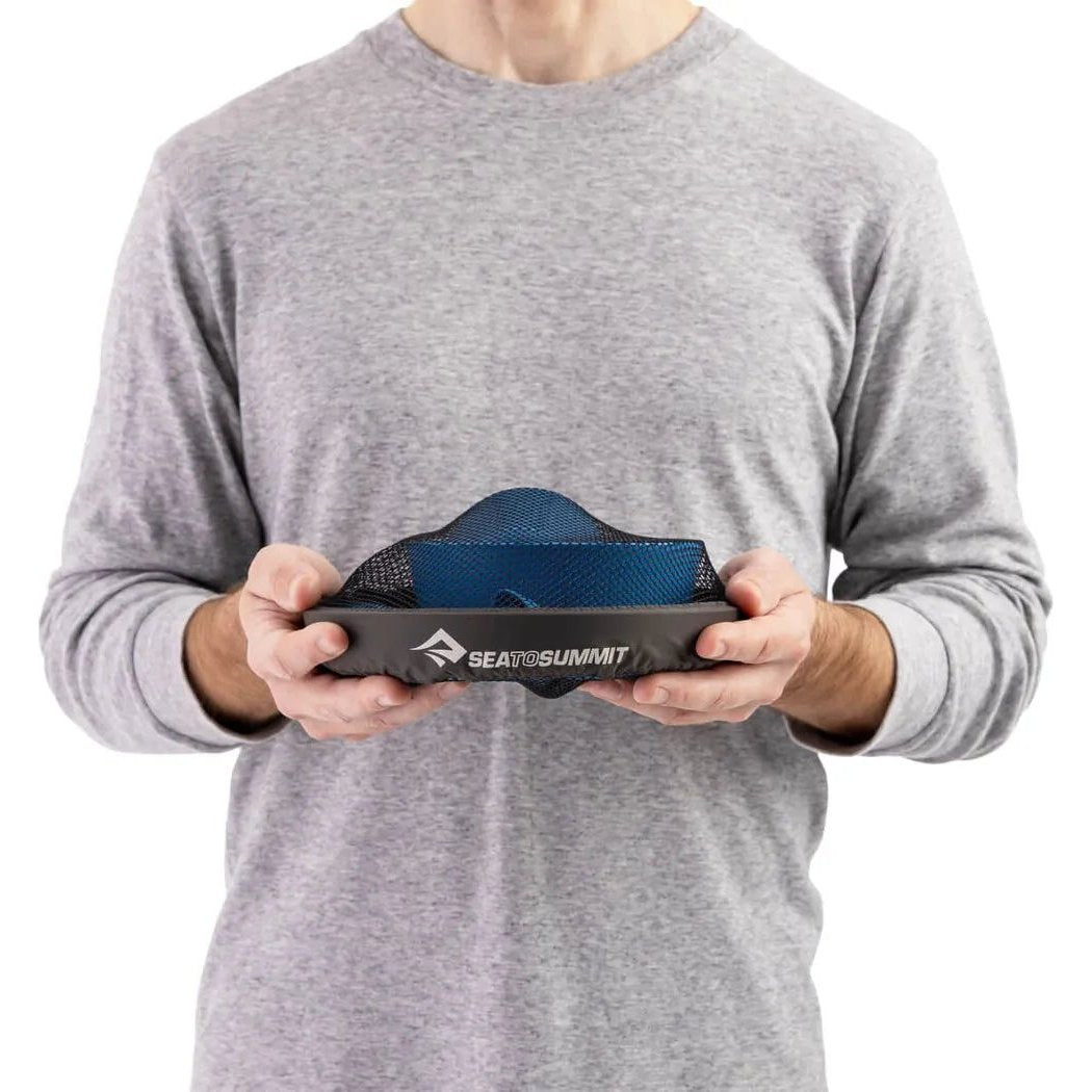 A person in a gray shirt holds the Sea To Summit Camp Dinnerware Set w/ Mesh Sack in Burnt Orange against a white background.