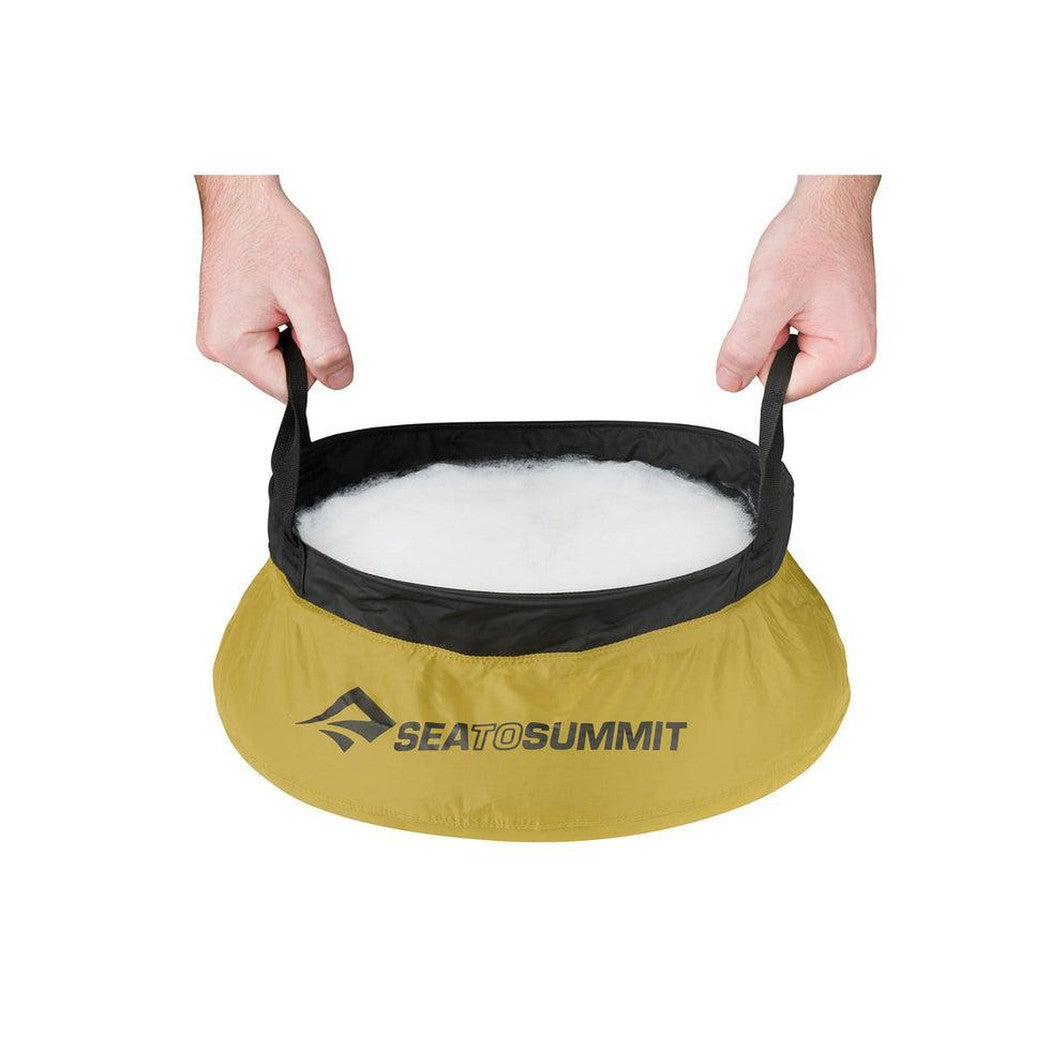A Sea To Summit Camp Kitchen Clean-Up Kit in yellow with black trim, held by hands against a white background.