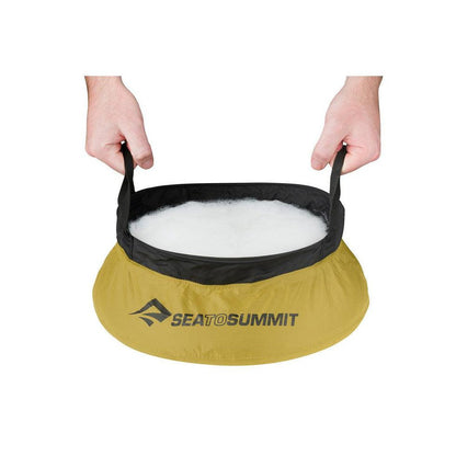 A Sea To Summit Camp Kitchen Clean-Up Kit in yellow with black trim, held by hands against a white background.