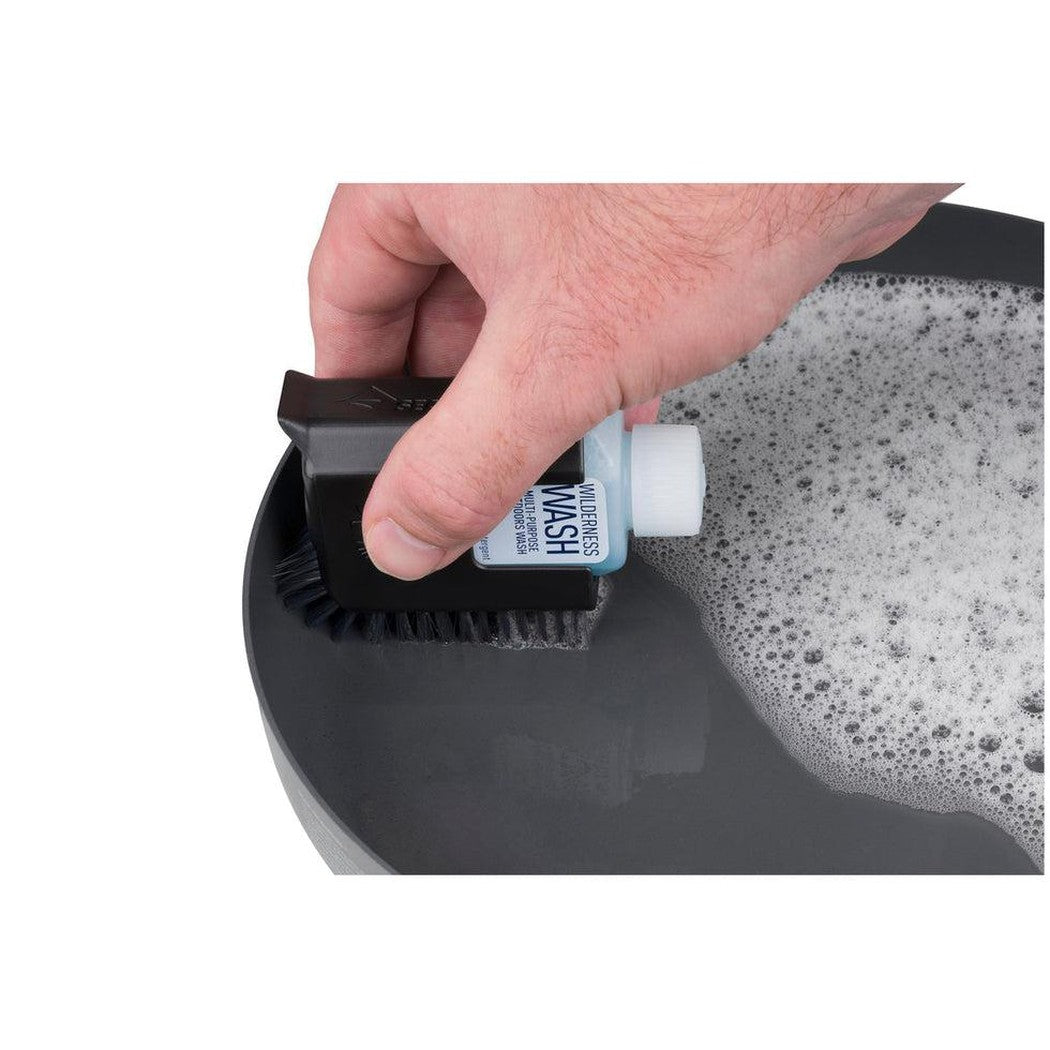 A hand uses the Sea To Summit Camp Kitchen Clean-Up Kit brush and wash bottle in a soapy basin.