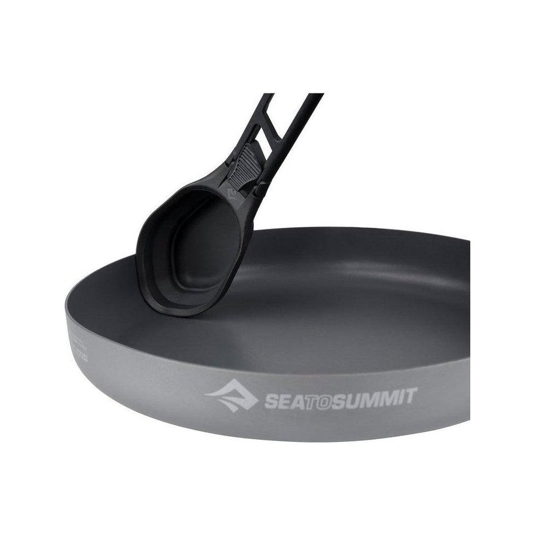 A close-up of the Sea To Summit Camp Kitchen Folding Serving Spoon resting on a charcoal-colored Sea To Summit plate.